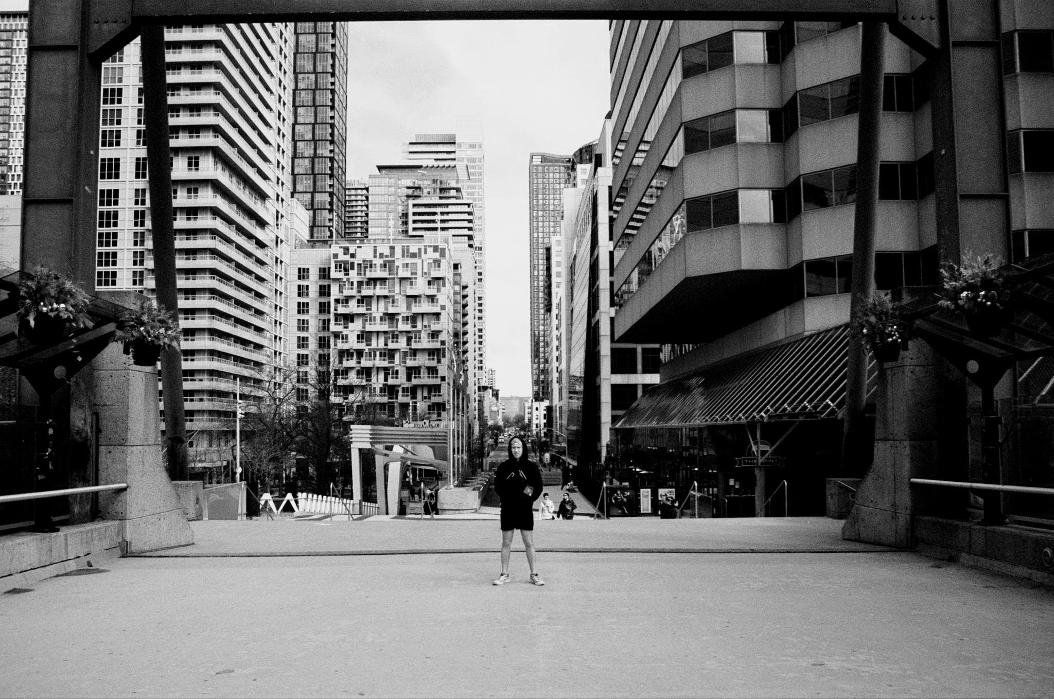 A person standing in an urban environment, surrounded by tall buildings, with a black and white aesthetic.